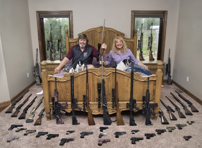 Middle-aged couple sitting on bed surrounded by guns