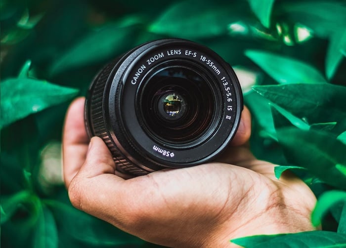 Hand holding a canon lens in a bush