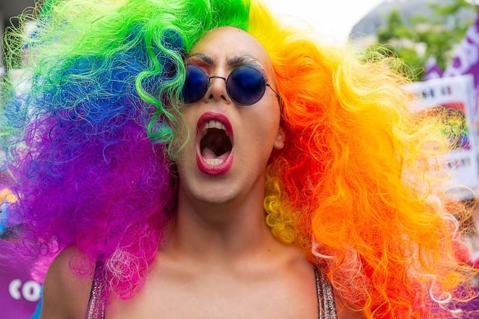 Trans person with sunglasses and a rainbow-colored wig