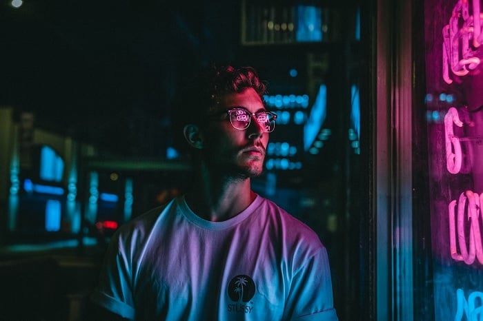 Portrait of a young man at night standing next to a pink neon sign