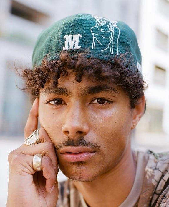 Portrait of a young man with curly hair under a backwards baseball cap
