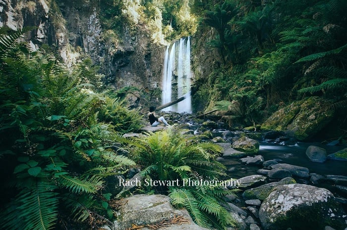 Woman sitting at foot of waterfall
