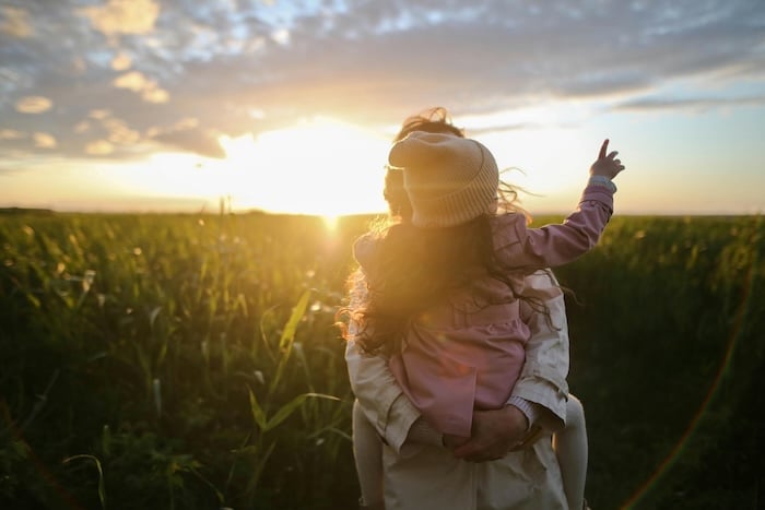 parent and child in a field during sunset