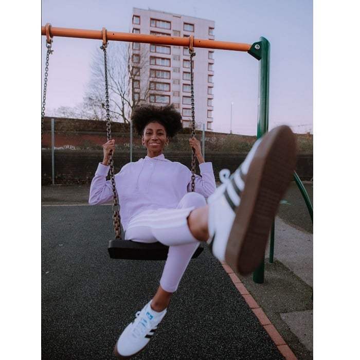 Young woman in pink Adidas tracksuit on swings below tower block