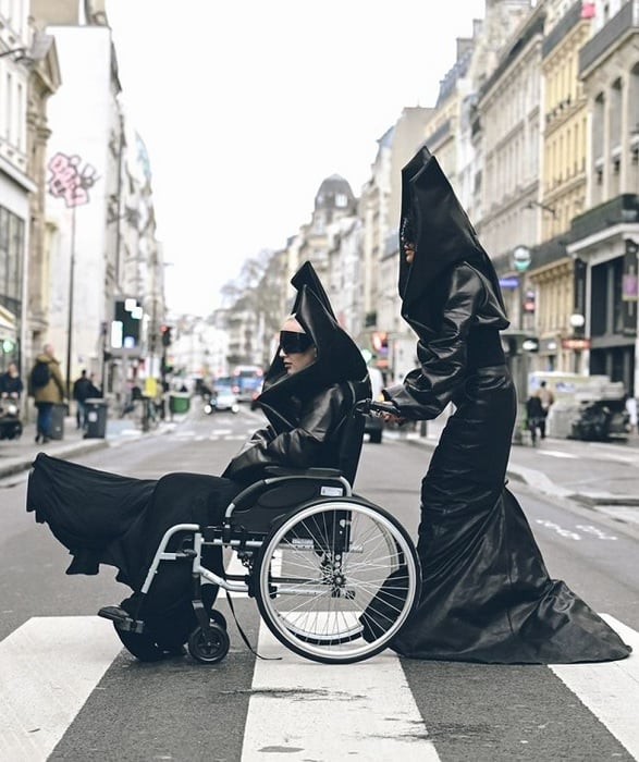 Person in a wheelchair being pushed by another person both dressed in black