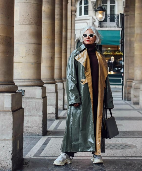 Woman under colonnade in long coat and sunglasses