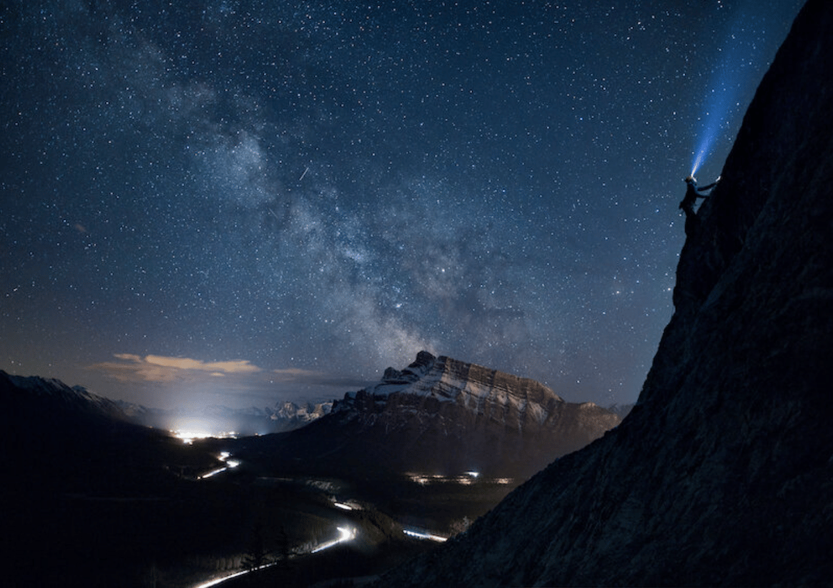 photograph of mountain range at night with climber with head torch 