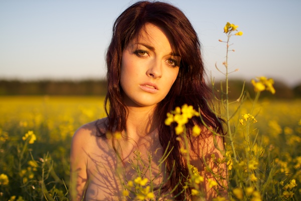 Foto de uma jovem no campo de flores amarelas, olhando para a câmera