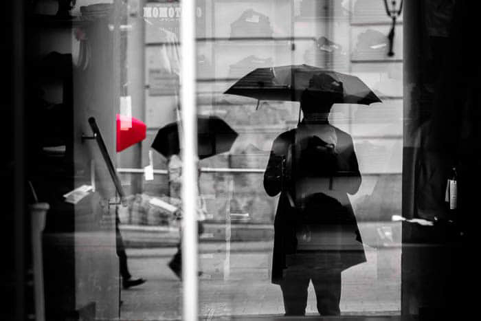 Μια ασπρόμαυρη φωτογραφία του δρόμου των ανθρώπων που περπατούν στη βροχή, μια ομπρέλα έχει κόκκινο χρώμα