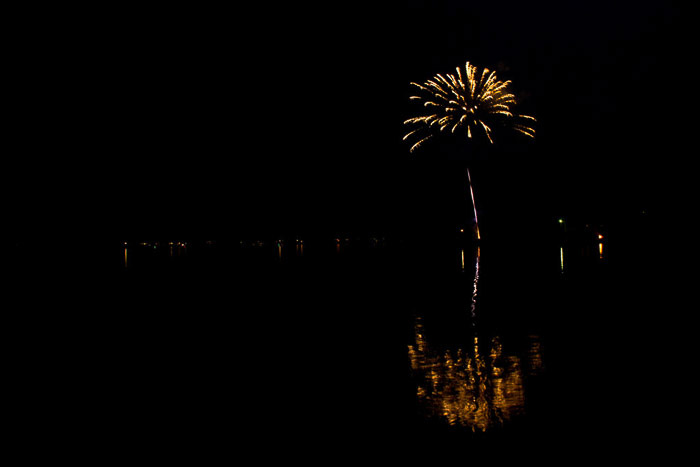 Foto incrível de fogos de artifício amarelos explodindo sobre a água à distância