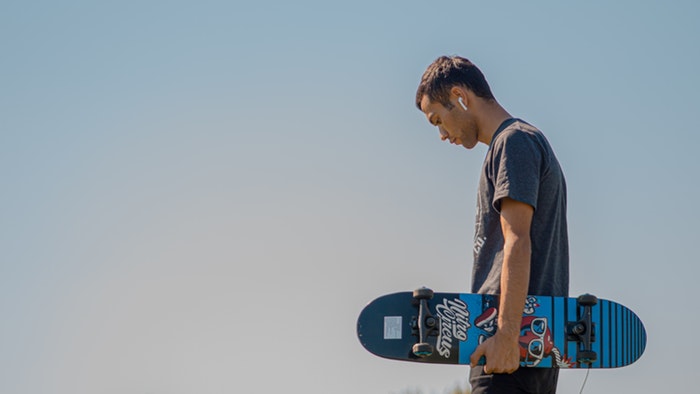 Homem segurando um skate contra um céu azul