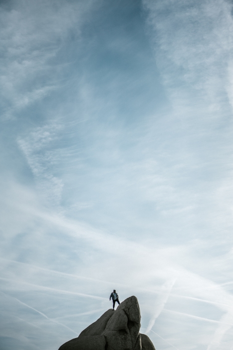 en person, der står på en klippe, med en blå himmel bag sig
