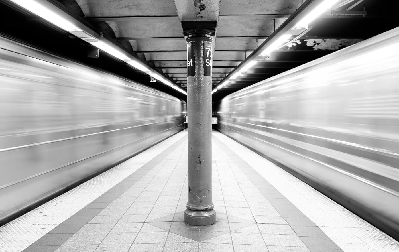 NYC tunnelbanetåg rusar förbi på båda sidor av plattformen, vilket skapar suddigt utrymme runt centrum