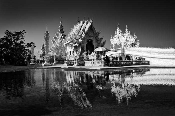 Fotografia de viagem em preto e branco do Templo Branco em Chiang Rai, Tailândia, o edifício refletido na água abaixo de 