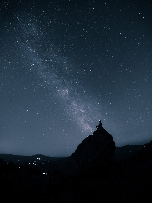 Foto impressionante de astrofotografia de um céu estrelado sobre a silhueta de um homem em uma rocha