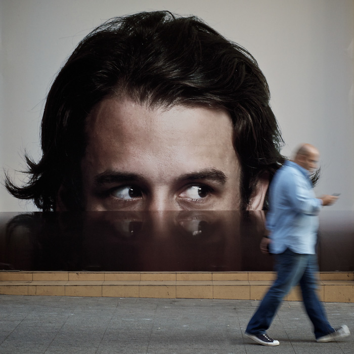 Os olhos em um anúncio parecem seguir um homem andando - fotografia de rua 