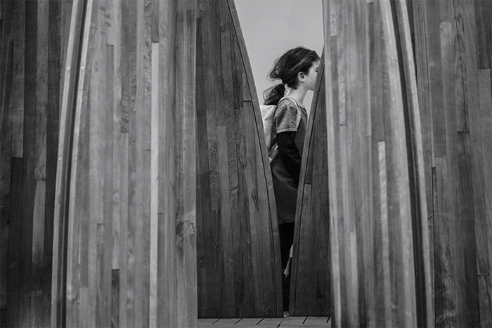 Foto em preto e branco de uma garota caminhando entre algumas tábuas de madeira