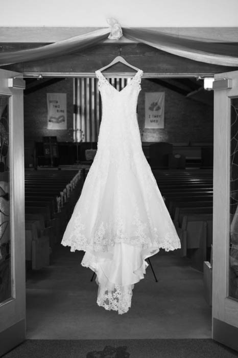 Een zwart-wit trouwfoto van een trouwjurk die boven de kerkdeuren hangt