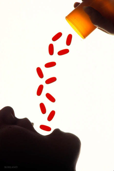 Una foto de stock conceptual de una persona vertiendo píldoras rojas en su boca