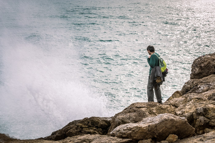 en ensom figur som står på steiner ved stranden og stirrer i vannet