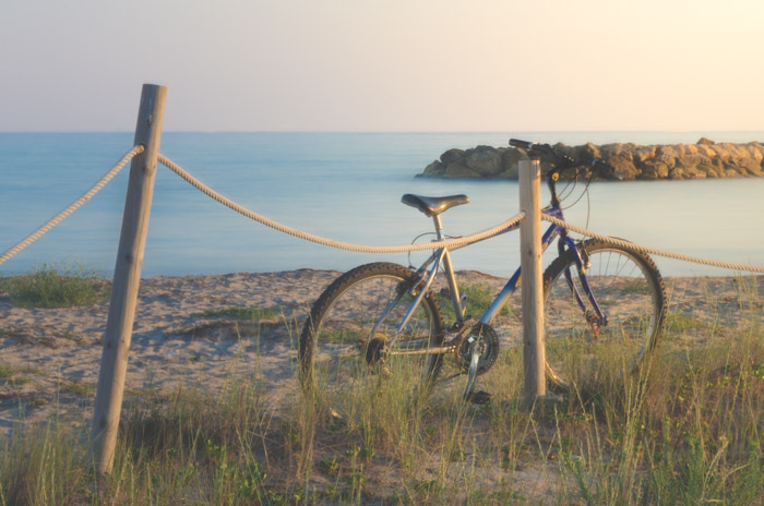 et drømmende foto af en cykel, der hviler mod et træhegn med havet i baggrunden