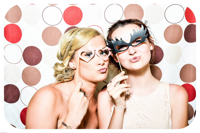 Duas garotas posando com máscaras em frente a um fundo fotográfico colorido