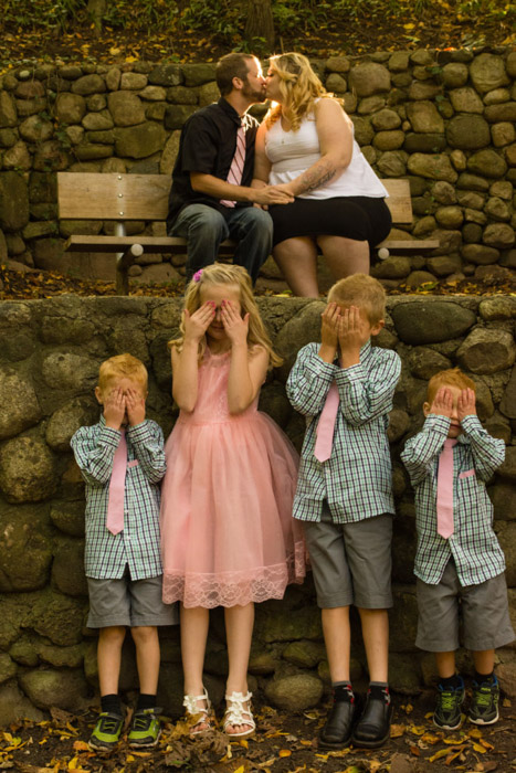 Cue a foto de família de quatro crianças protegendo os olhos dos pais beijando atrás deles