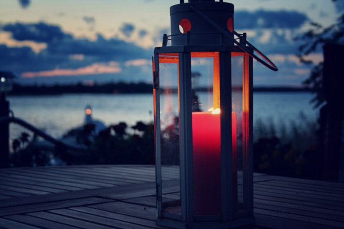 Vela vermelha acesa dentro de uma lanterna em uma mesa de madeira ao lado de um lago ao pôr do sol