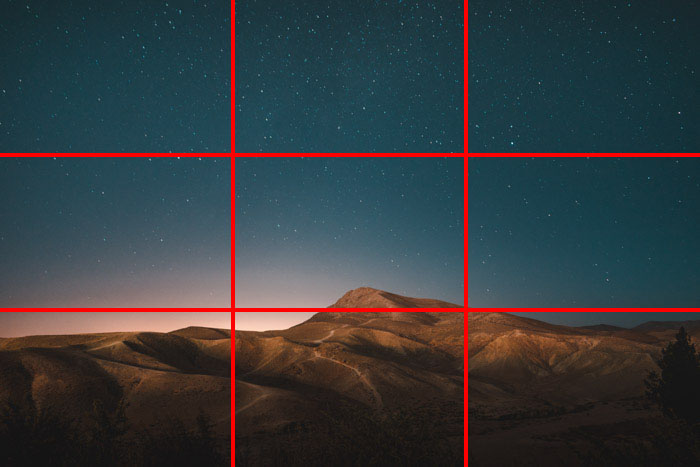 A mountainous scene with a stunning star filled night sky above, with the rule of thirds composition grid overlayed