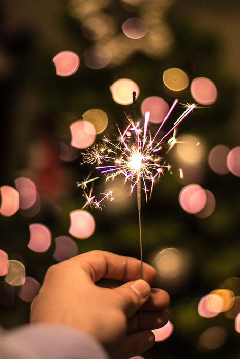 Macro immagine di una mano che tiene una scintilla accesa di notte. Fotografia con poca luce.