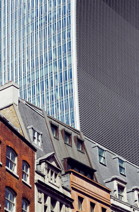 Photo of houses in mixed architectural styles in the foreground in juxtaposition to a huge skyscraper in the background .