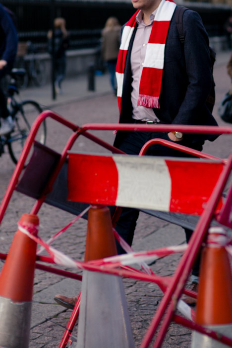 fotografia uliczna mężczyzny w szaliku przypominającym otoczenie w barierkach drogowych i taśmach.