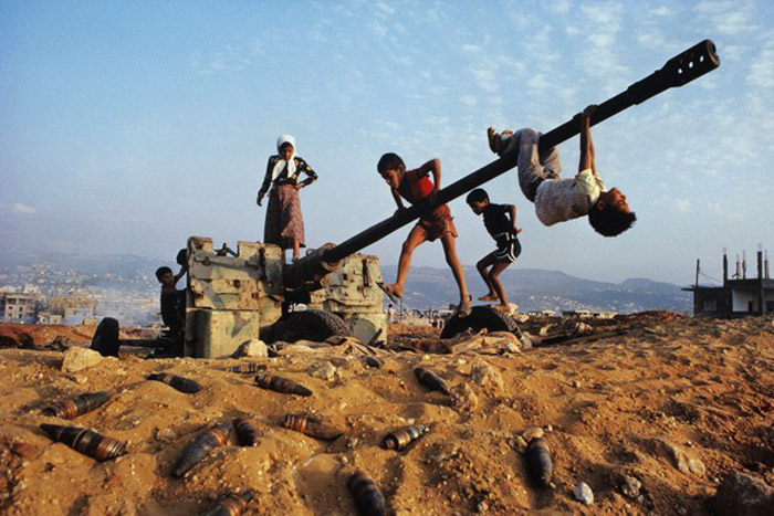 Fotografía documental de niños jugando alrededor de un arma de artillería abandonada y en desuso.