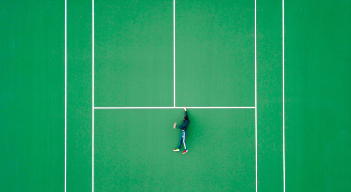 Overhead foto af en mand på en tennisbane, men ser ud som om han holder fast i en afsats for kære liv