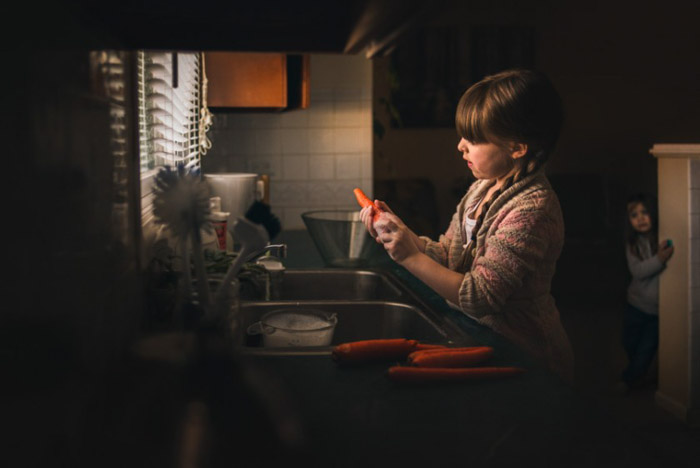 et foto af en lille pige, der skræller gulerødder ved køkkenvasken