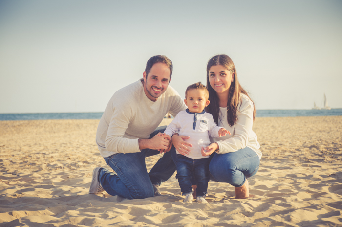 Uma sessão de fotos de família de um casal e um bebê posando na praia 