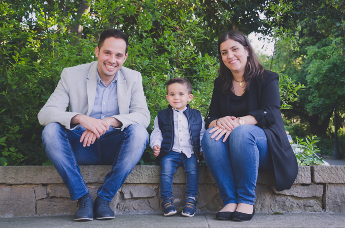 Foto de família de um casal e um filho sentado em uma parede ao ar livre 