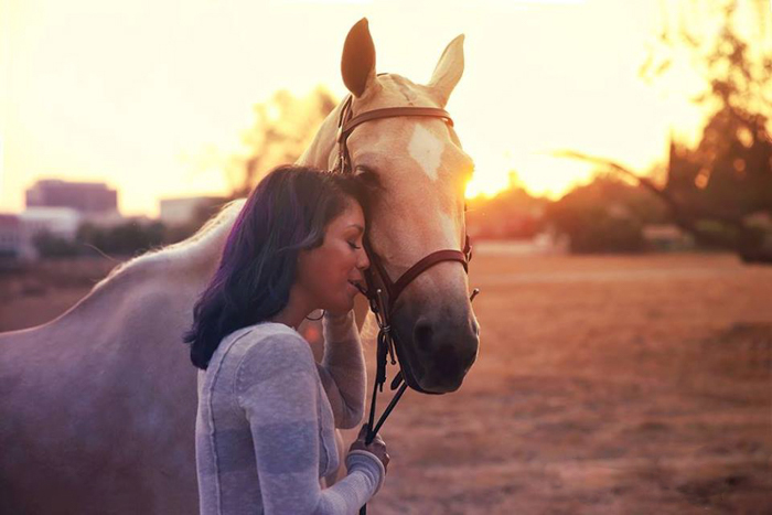 A girl pressing her forehead against a light brown horse at evening time