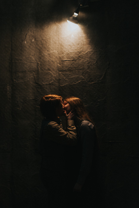 A couple kissing in front of a textured wall with a single light source 