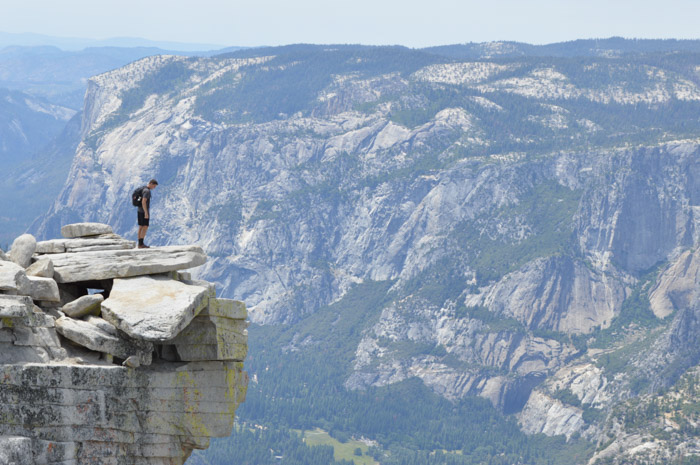 Um homem parado na beira de um penhasco com uma paisagem montanhosa deslumbrante atrás dele, demonstrando o equilíbrio entre tamanho e peso na fotografia
