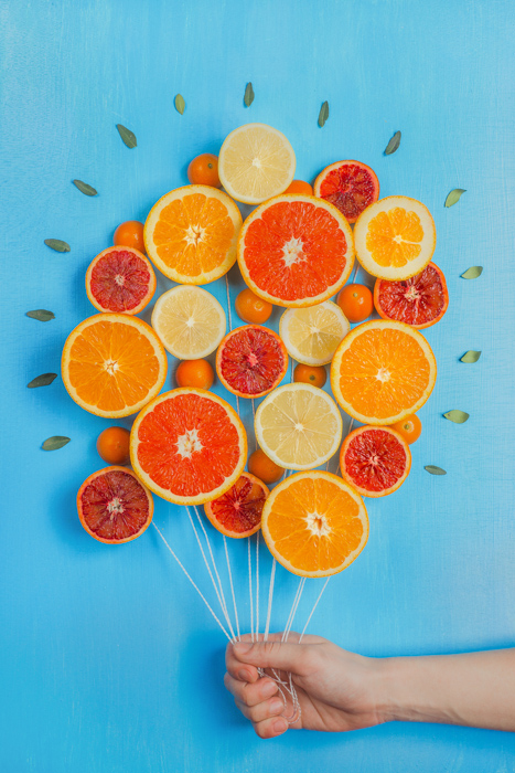 Un arreglo de ideas de fotografía de naturaleza muerta de naranjas hechas para que parezcan un montón de globos, sobre fondo azul