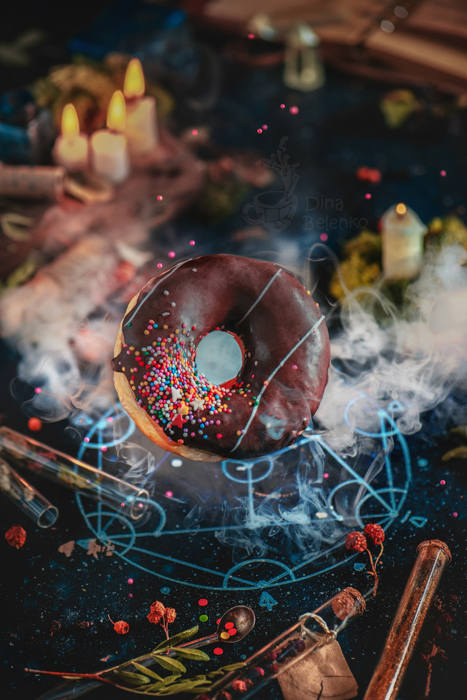 Idee di fotografia still life di ciambella glassata al cioccolato volante evocata con un pentagramma alchemico