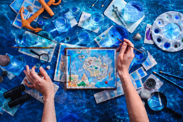 Overhead shot de um artista pintando um mapa de ilha de fantasia. Ideias de fotografia subaquática de natureza morta