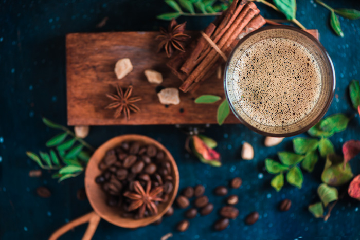 uma parte superior ainda viva de chávenas de café, grãos de café, paus de canela e folhagem numa tábua de madeira