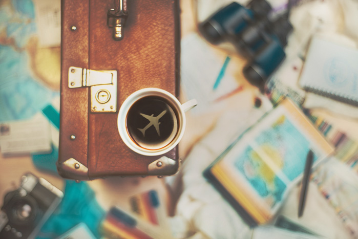 Overhead-Aufnahme einer Kaffeetasse mit dem Bild eines Flugzeugs im Inneren, das auf einem Koffer ruht