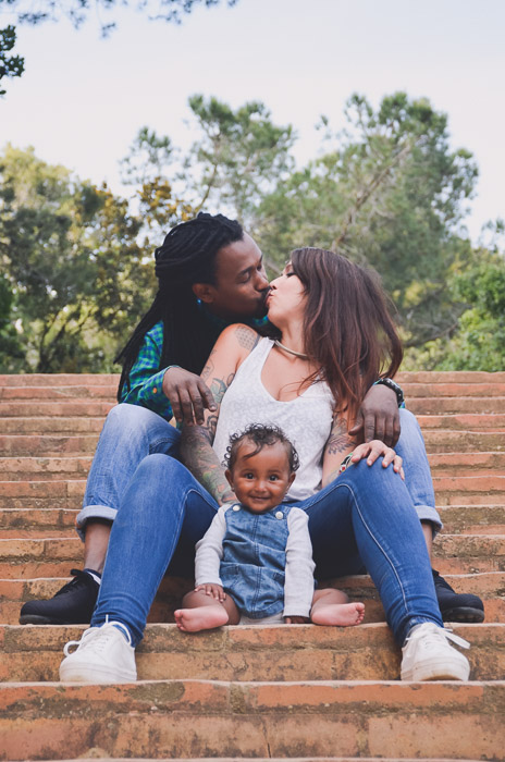 Foto de retrato de família de um casal e um bebê sentado nos degraus ao ar livre.