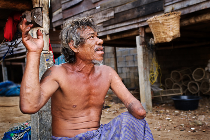 een milieuportretfoto van een Moken sea gypsie man in Zuid-Thailand die ons vertelt hoe hij zijn hand verloor. 
