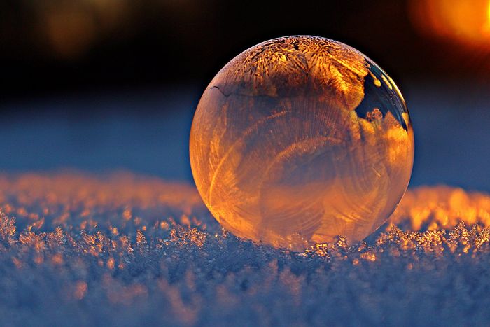 Nahaufnahme einer Seifenblase, in der sich Schneeflocken spiegeln