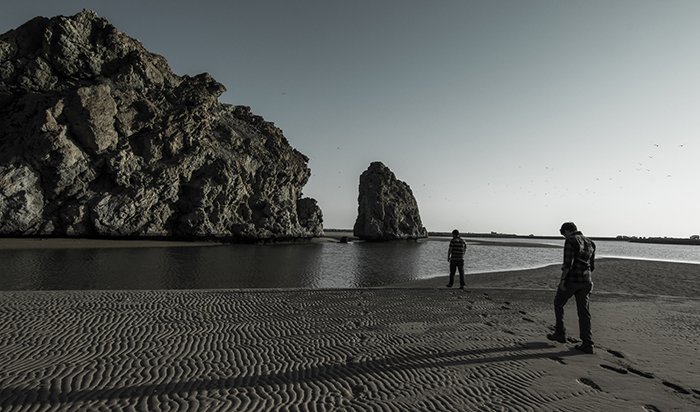 Une photographie d'art en noir et blanc d'une plage rocheuse, avec un doux effet brumeux de l'eau autour des rochers et des falaises