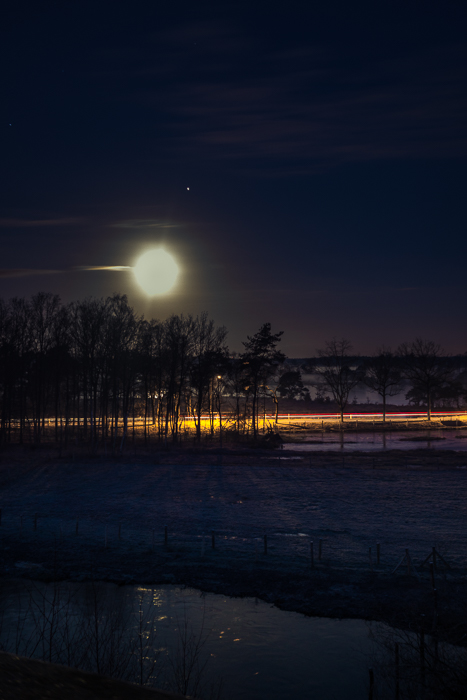 licht trails in a winter night under a full Moon (with Jupiter next it).